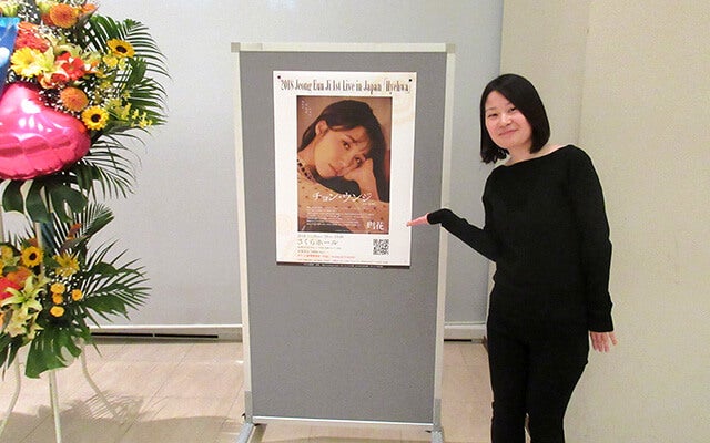 コンサートポスターの前で記念撮影する石渡さん